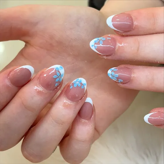 White french tips with hand-painted blue flowers, by Nails First Garston
